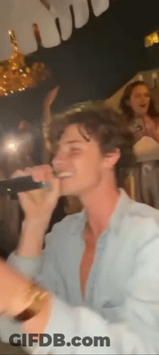 A Man Is Singing Into A Microphone At A Party In A Dark Room . GIF