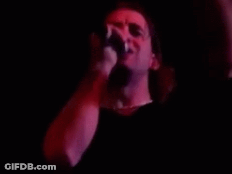 A Man Is Singing Into A Microphone In A Dark Room With Red Lights . GIF