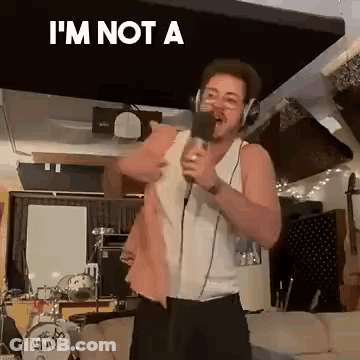 A Man Is Singing Into A Microphone In A Living Room While Wearing Headphones . GIF
