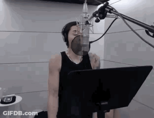 A Man Is Singing Into A Microphone In A Recording Studio While Wearing Headphones . GIF