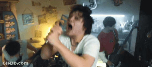 A Man Is Singing Into A Microphone In A Room With Other People GIF
