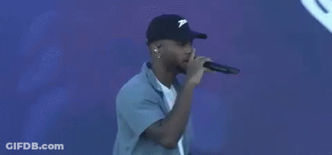 A Man Is Singing Into A Microphone In Front Of A Blue Background With A Heart . GIF