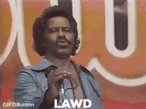 A Man Is Singing Into A Microphone In Front Of A Large Sign . GIF