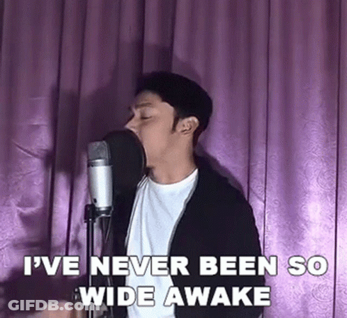 A Man Is Singing Into A Microphone In Front Of A Pink Curtain . GIF