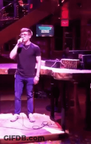 A Man Is Singing Into A Microphone In Front Of A Sign That Says No Smoking Served GIF