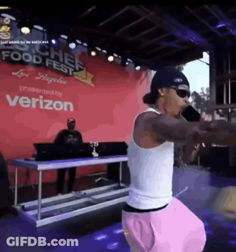 A Man Is Singing Into A Microphone In Front Of A Verizon Sign GIF