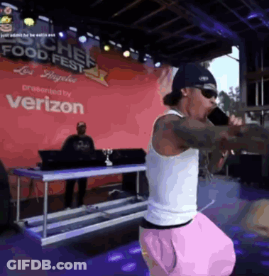 A Man Is Singing Into A Microphone In Front Of A Verizon Sign GIF