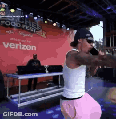 A Man Is Singing Into A Microphone In Front Of A Verizon Sign GIF