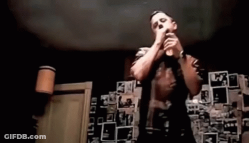 A Man Is Singing Into A Microphone In Front Of A Wall Covered In Pictures . GIF
