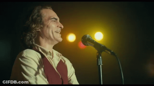 A Man Is Singing Into A Microphone In Front Of A Yellow Light . GIF