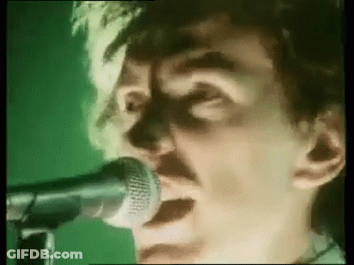 A Man Is Singing Into A Microphone On A Green Background . GIF