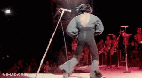 A Man Is Singing Into A Microphone On A Stage . GIF