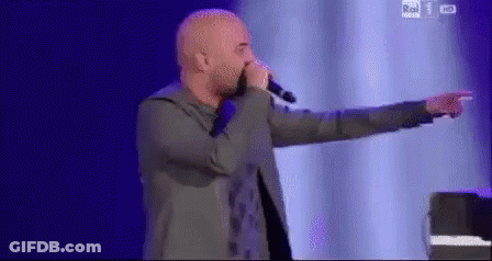 A Man Is Singing Into A Microphone On A Stage And Pointing At Something . GIF