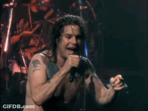 A Man Is Singing Into A Microphone On A Stage GIF