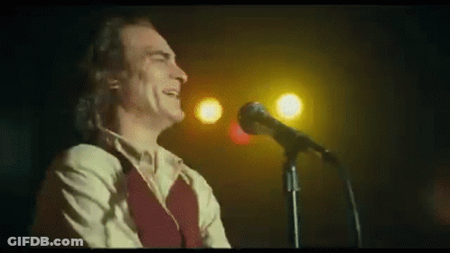 A Man Is Singing Into A Microphone On A Stage In A Dark Room . GIF