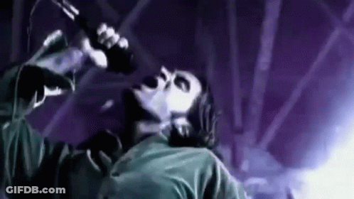 A Man Is Singing Into A Microphone On A Stage In A Dark Room . GIF