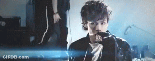 A Man Is Singing Into A Microphone On A Stage In Front Of A Crowd . GIF