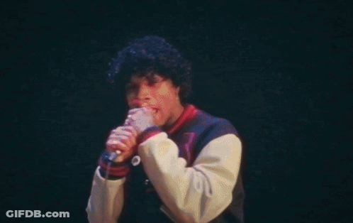 A Man Is Singing Into A Microphone On A Stage In Front Of A Crowd . GIF