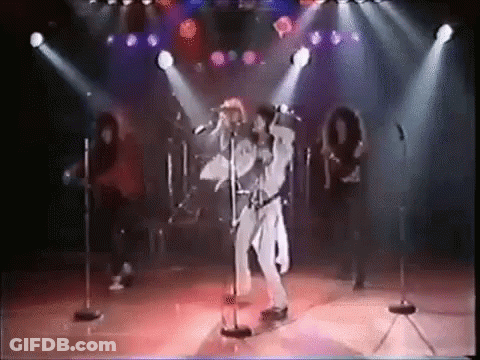 A Man Is Singing Into A Microphone On A Stage In Front Of A Group Of People . GIF
