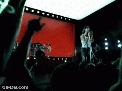 A Man Is Singing Into A Microphone On A Stage In Front Of A Red Curtain . GIF