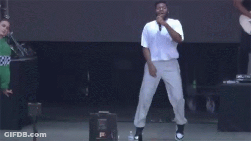 A Man Is Singing Into A Microphone On A Stage While Dancing . GIF