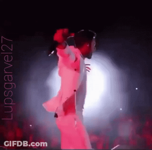 A Man Is Singing Into A Microphone On A Stage With A Crowd Behind Him . GIF