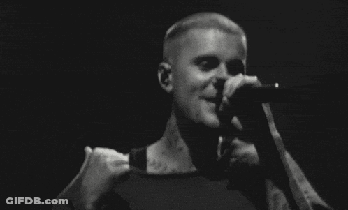 A Man Is Singing Into A Microphone On Stage In A Black And White Photo . GIF