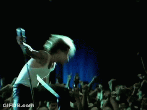 A Man Is Singing Into A Microphone On Stage In Front Of A Crowd . GIF