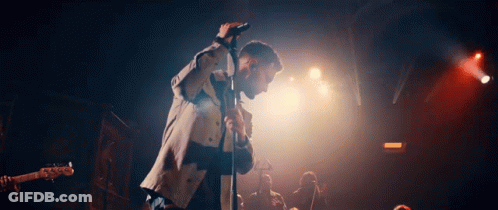 A Man Is Singing Into A Microphone On Stage In Front Of A Crowd GIF