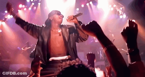 A Man Is Singing Into A Microphone On Stage In Front Of A Crowd Of People . GIF