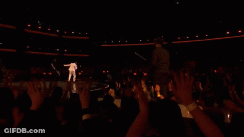 A Man Is Singing Into A Microphone While Another Man Plays A Guitar Behind Him . GIF