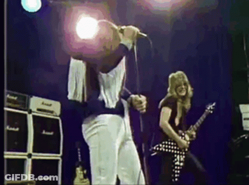 A Man Is Singing Into A Microphone While Another Man Plays A Guitar On Stage . GIF