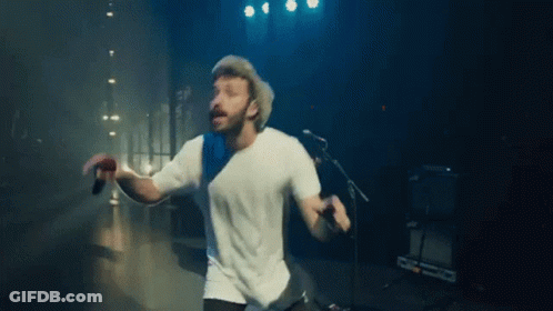 A Man Is Singing Into A Microphone While Dancing On A Stage . GIF