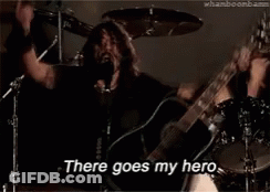 A Man Is Singing Into A Microphone While Holding A Guitar And Saying There Goes My Hero GIF