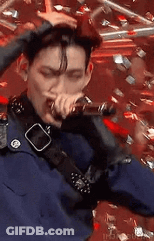 A Man Is Singing Into A Microphone While Holding His Hair . GIF