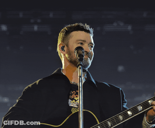 A Man Is Singing Into A Microphone While Playing A Guitar GIF