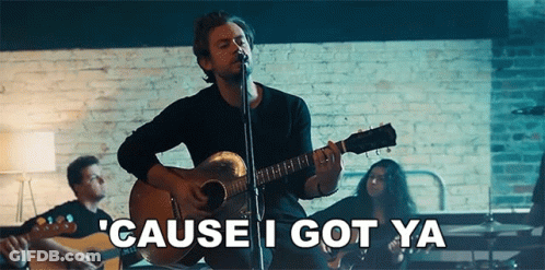 A Man Is Singing Into A Microphone While Playing A Guitar In Front Of A Brick Wall . GIF