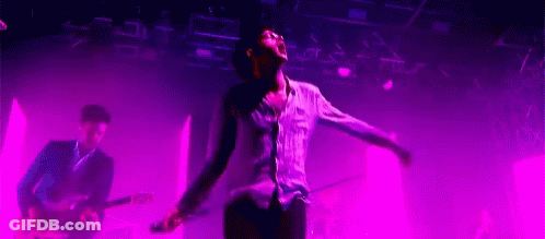 A Man Is Singing Into A Microphone While Playing A Guitar On Stage . GIF