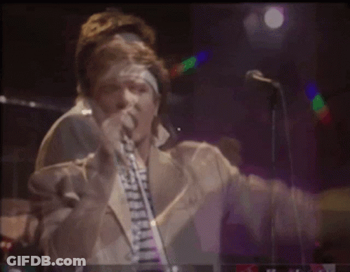 A Man Is Singing Into A Microphone While Playing A Guitar On Stage GIF