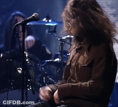 A Man Is Singing Into A Microphone While Playing Drums GIF