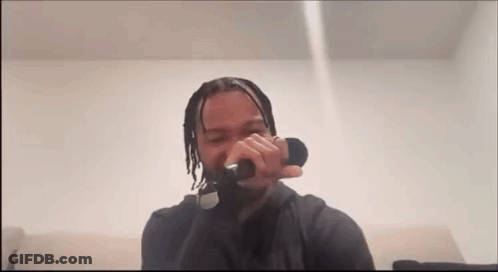 A Man Is Singing Into A Microphone While Sitting On A Couch In A Room . GIF