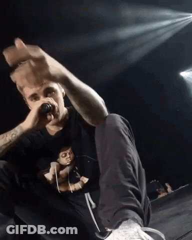 A Man Is Singing Into A Microphone While Sitting On A Stage GIF