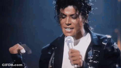 A Man Is Singing Into A Microphone While Wearing A Black Jacket GIF