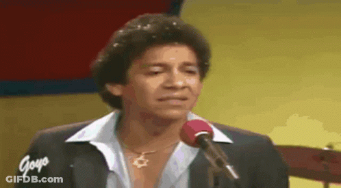 A Man Is Singing Into A Microphone While Wearing A Necklace . GIF