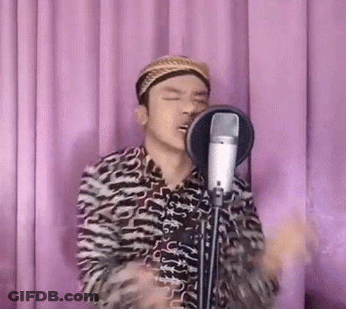 A Man Is Singing Into A Microphone While Wearing A Turban . GIF