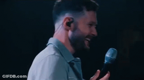 A Man Is Singing Into A Microphone While Wearing Earbuds . GIF