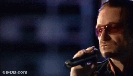 A Man Is Singing Into A Microphone While Wearing Sunglasses . GIF