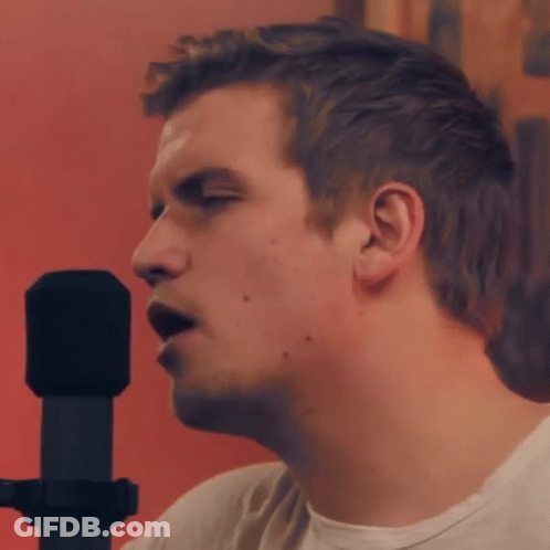 A Man Is Singing Into A Microphone With A Red Background GIF