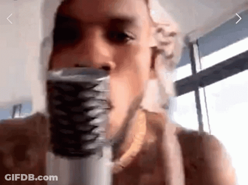 A Man Is Singing Into A Microphone With A Window Behind Him GIF