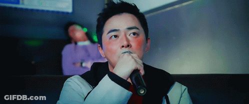 A Man Is Singing Into A Microphone With His Hand On His Chin GIF